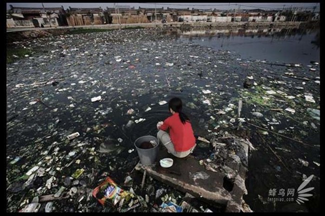 Chinese villager washing clothes in a contaminated river.