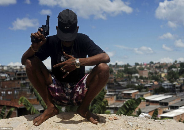 Cujas ruas?  Um membro de uma gangue de drogas brasileiro apelidado de foguete, 22, posa com uma arma em cima de uma colina com vista para uma favela de Salvador Leia mais: